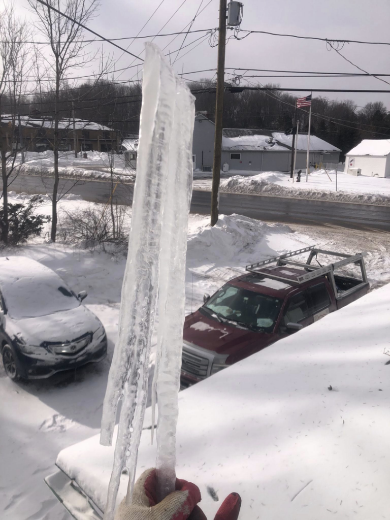 A worker performing ice removal services, holding a large icicle, for Manny General Construction Llc in Scranton, PA.