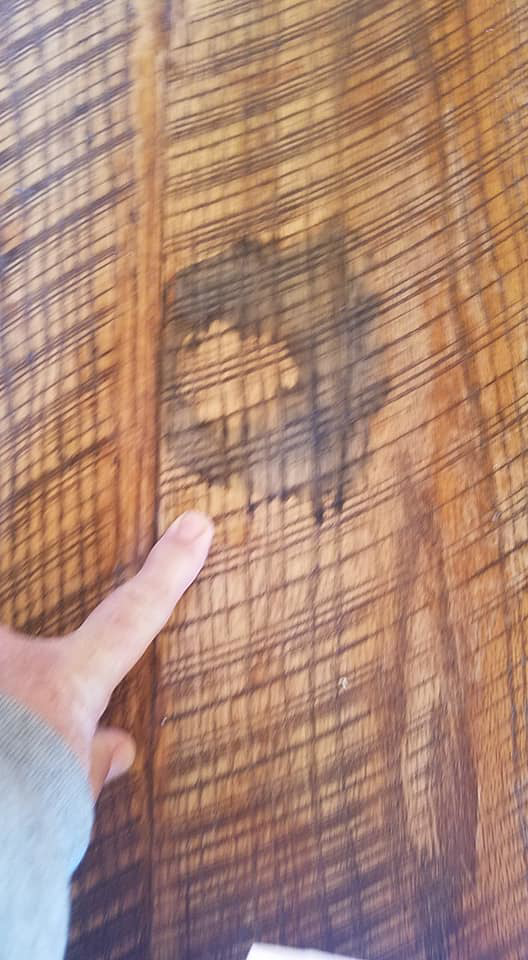 A finger pointing at a dark stain or water damage on a wooden surface, identified by Bevard Enterprises in Millcreek, UT.