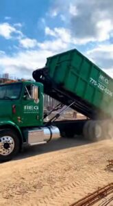 An IEG Disposal truck delivering or picking up a green roll-off dumpster at a construction site in Canton, GA.