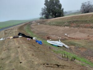An illegal dumping site with a discarded boat, mattress, and various debris along a roadside, requiring cleanup by Valley Haul Off LLC in Visalia, CA.
