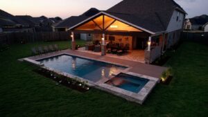 An illuminated backyard pool, spa, and covered patio at dusk, designed by Limitless Custom Pools and Backyards in Houston, TX.