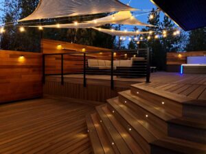 A beautifully illuminated deck at dusk with string lights and built-in stair lighting, designed by Ridgeline Decks in Spokane, WA.
