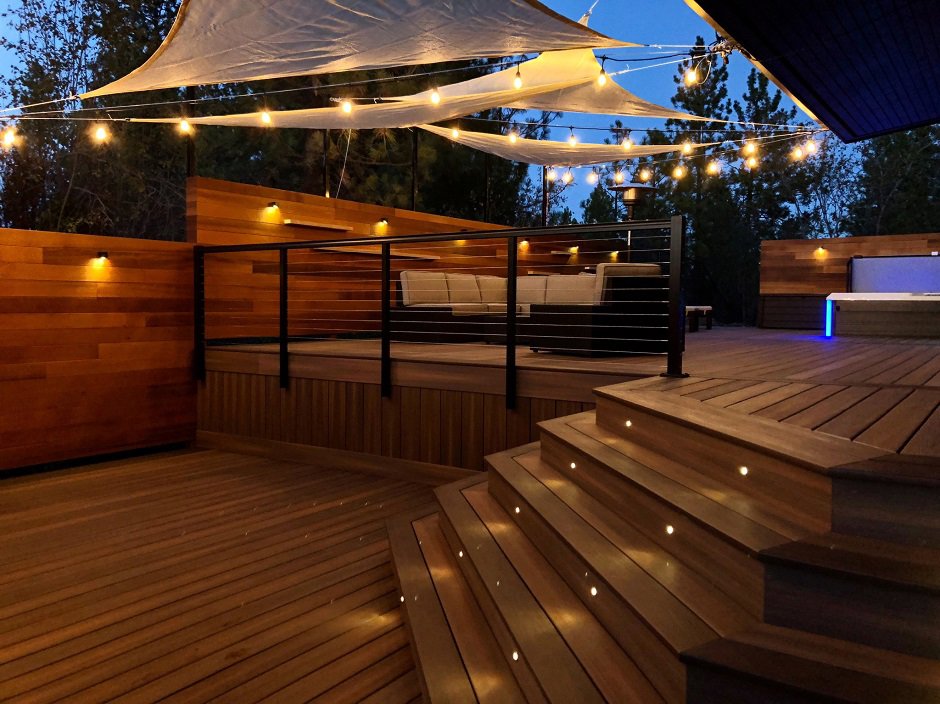 A beautifully illuminated deck at dusk with string lights and built-in stair lighting, designed by Ridgeline Decks in Spokane, WA.