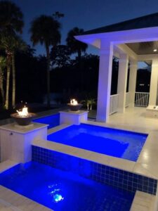 An illuminated pool area at night with vibrant blue lighting and decorative fire features, a project by TamLin Homes Inc in Tampa, FL