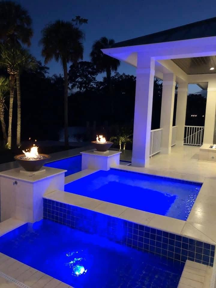 An illuminated pool area at night with vibrant blue lighting and decorative fire features, a project by TamLin Homes Inc in Tampa, FL