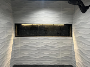 A close-up view of an illuminated shower niche with textured white wall tiles installed by Patriot Tile LLC in Skiatook, OK.