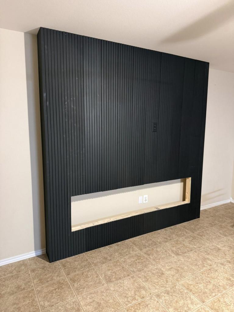 An in-progress slatted wall installation showing the opening for an electric fireplace by Camacho's Construction LLC in Laredo, TX.