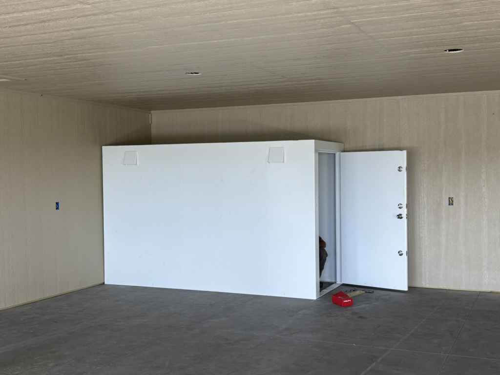 A newly installed white indoor storm shelter with its door open inside a garage by Enid Storm Shelters in Enid, OK.