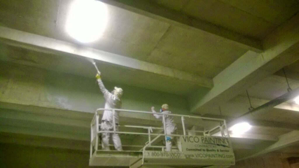 Workers in a scissor lift performing industrial ceiling painting for Vico Painting Contractors in Hialeah, FL