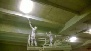 Workers in a scissor lift performing industrial ceiling painting for Vico Painting Contractors in Hialeah, FL