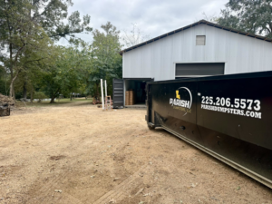 An industrial dumpster from Parish Dumpsters, LLC placed near a large metal building in Baton Rouge, LA.