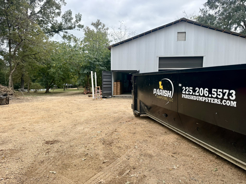 An industrial dumpster from Parish Dumpsters, LLC placed near a large metal building in Baton Rouge, LA.