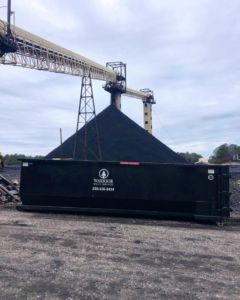 A black roll-off dumpster from Warrior Waste Services at an industrial site in Northport, AL.