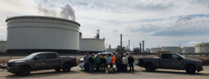 A team of workers from Jason Mechanical Corp standing in front of large industrial tanks and a refinery in Joliet, IL, showcasing their general contractor work.