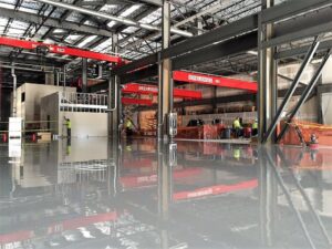 An industrial warehouse with a grey epoxy floor and red overhead cranes by Heavy Duty Floors, LLC in New Britain, CT.