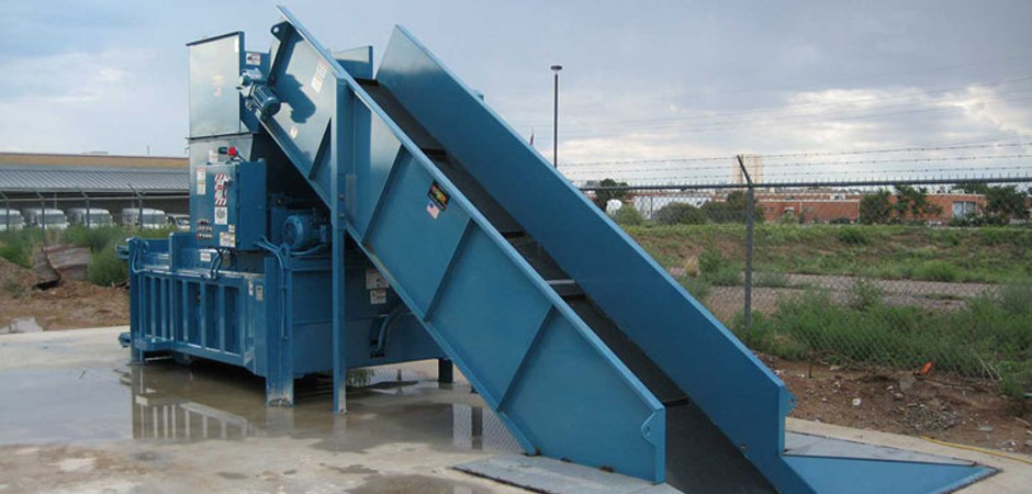 A large blue industrial waste compactor with an inclined conveyor at Jackson Compaction in Albuquerque, NM.