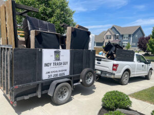 An Indy Trash Guy branded truck and trailer loaded with furniture and various junk items for removal in Fishers, IN.