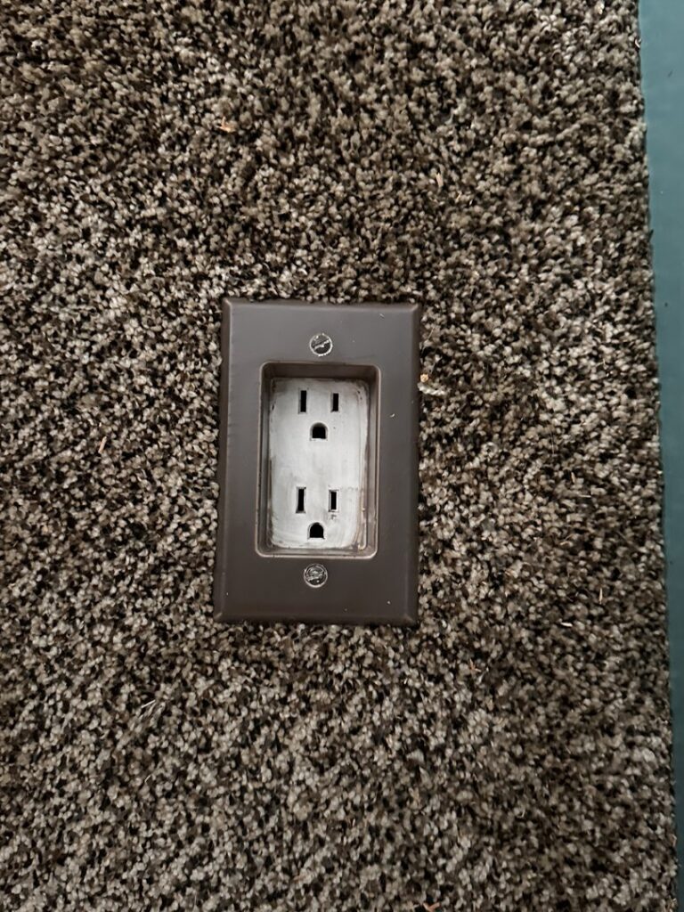 A close-up view of a newly installed floor electrical outlet on a carpeted floor by Green River Utilities in Caldwell, ID.