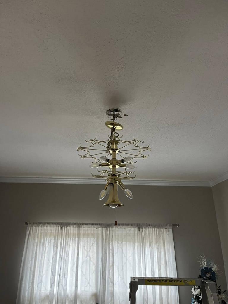 A handyman installing a ceiling chandelier light fixture for Task Tacklers Handyman Services in Olathe, KS.