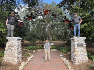 Handymen installing a decorative metal archway with rose details for a garden at Gowan Iron in Montgomery, AL.