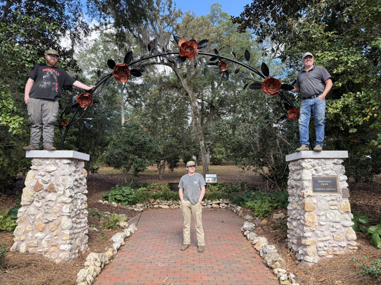 Handymen installing a decorative metal archway with rose details for a garden at Gowan Iron in Montgomery, AL.