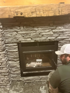A worker installing a new fireplace insert into a stone fireplace, a remodeling service by United Brothers Insulation and Remodeling in Athens, GA.