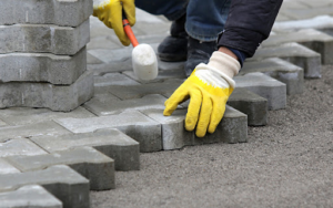Hands installing interlocking concrete pavers for a walkway or patio by Cervantes Concrete Llc in Caledonia, WI.
