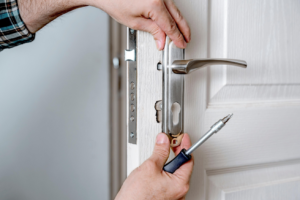 A handyman installing a modern door lock and handle assembly with a screwdriver for Door Tech of Nashville, Inc. in Nashville, TN.