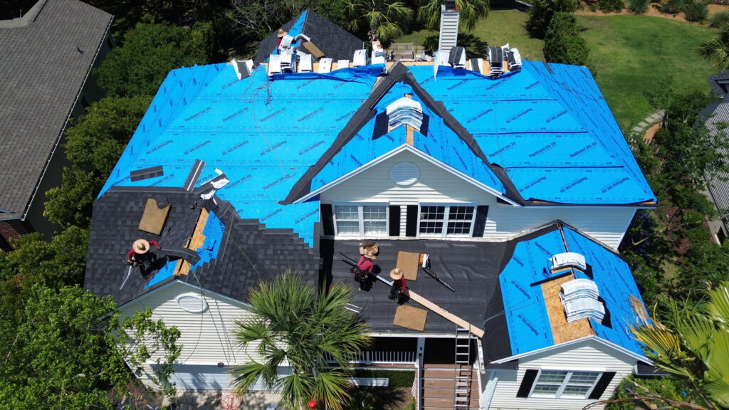 An aerial view of workers installing shingles and blue underlayment on a roof by Coastal Roofing Solutions LLC in Charleston, SC.