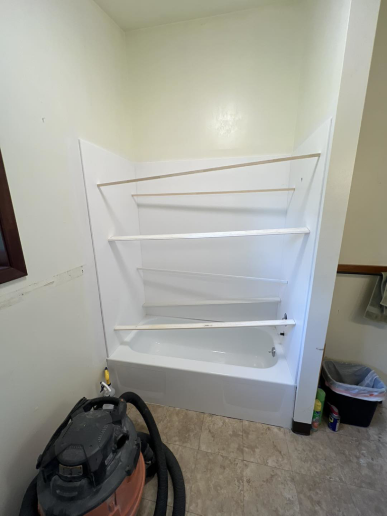 Handyman installing new shower surround panels over a bathtub during a bathroom remodel by JKM Services in Solon, OH.