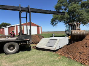 Workers installing an underground concrete storm shelter with a backhoe and crane for Enid Storm Shelters in Enid, OK.