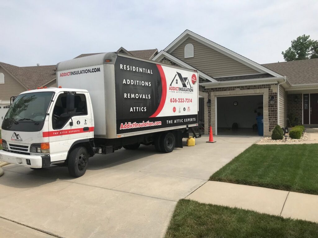 An ADDICT INSULATION, LLC truck with an insulation hose at a residential job site in St. Charles, MO.