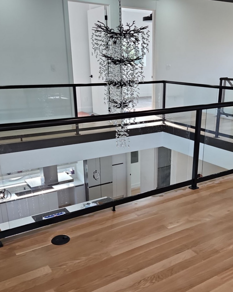 A second-floor interior balcony with stylish glass railings overlooking a modern kitchen, installed by Alpha Railing Company in Tacoma, WA.