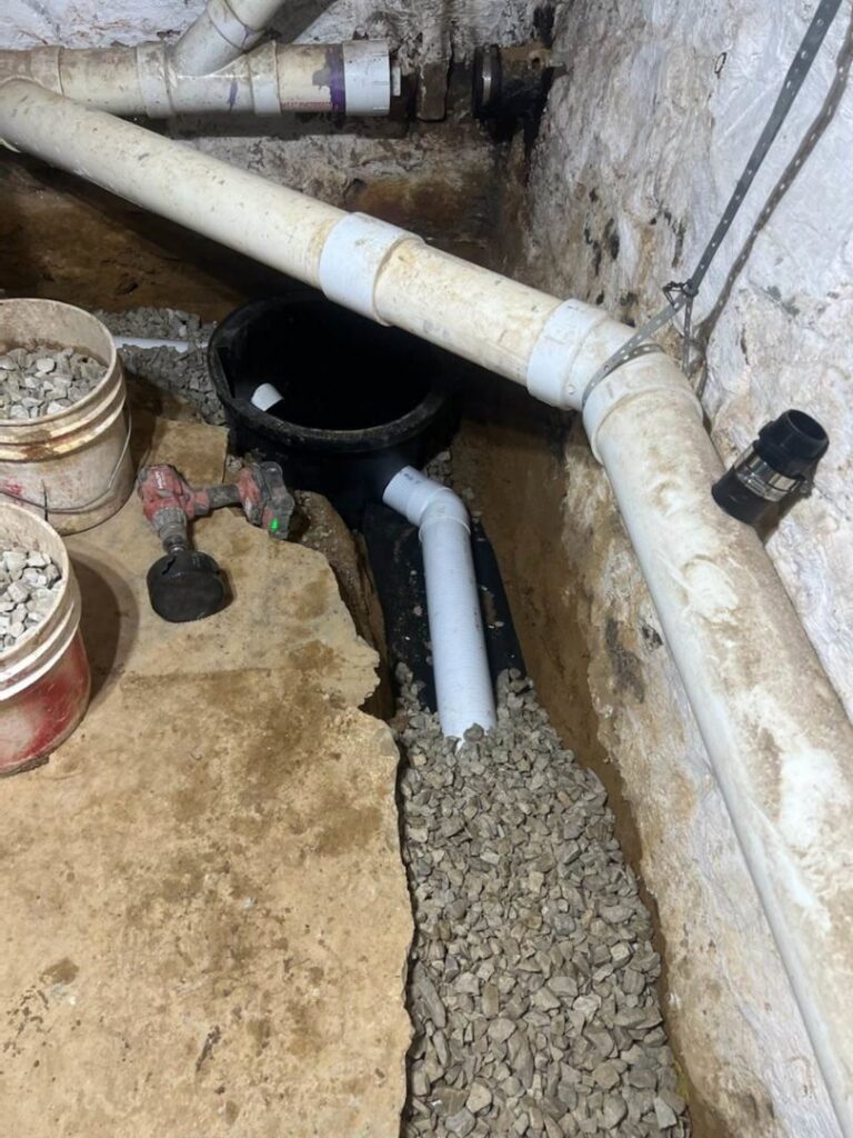 Installation of an interior basement drainage system with pipes, gravel, and a sump pump basin by Foundation Repair and Waterproofing in Philadelphia, PA.
