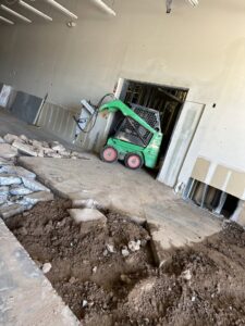 An interior demolition site with a green Bobcat and piles of rubble, indicating debris removal services by HAVOC Demolition in Scottsdale, AZ.