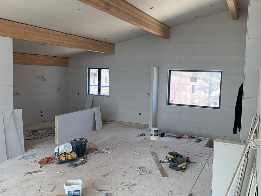 An interior room with newly installed drywall and exposed wooden beams, showing a construction site by Diamond Drywall in Colorado Springs, CO.