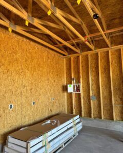 An interior view of a house under construction, featuring exposed wooden ceiling trusses and electrical wiring by Kelso Custom Builders, Inc. in Phoenix, AZ.