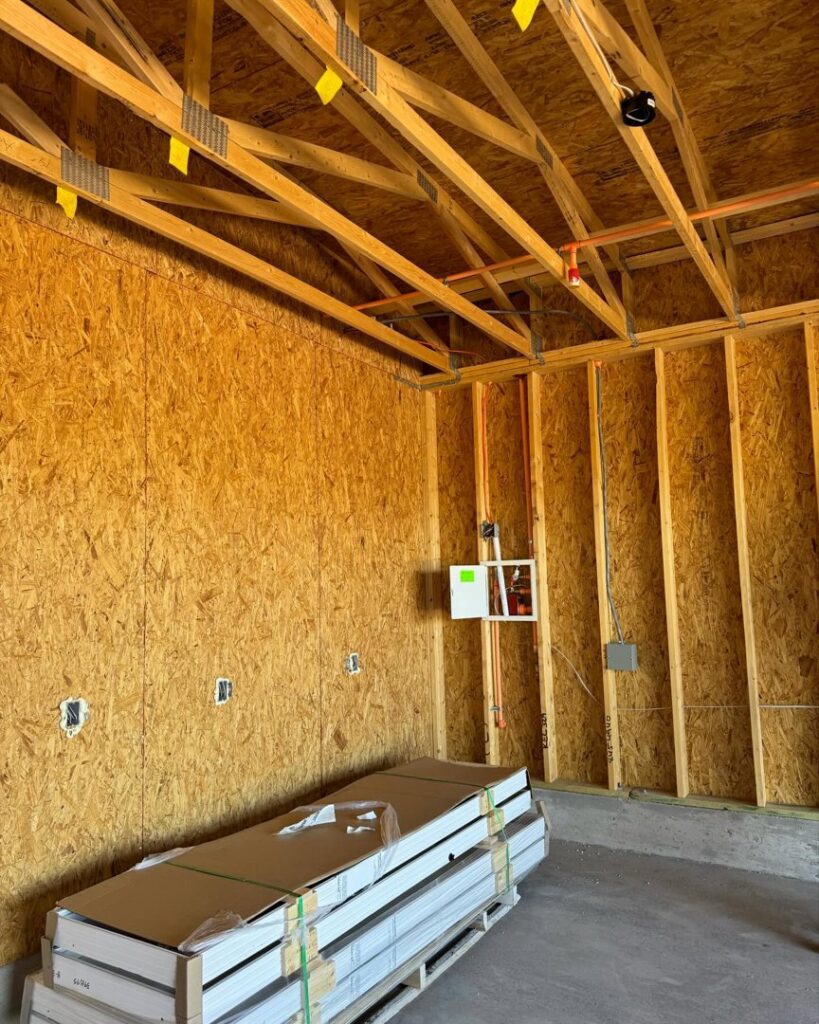 An interior view of a house under construction, featuring exposed wooden ceiling trusses and electrical wiring by Kelso Custom Builders, Inc. in Phoenix, AZ.