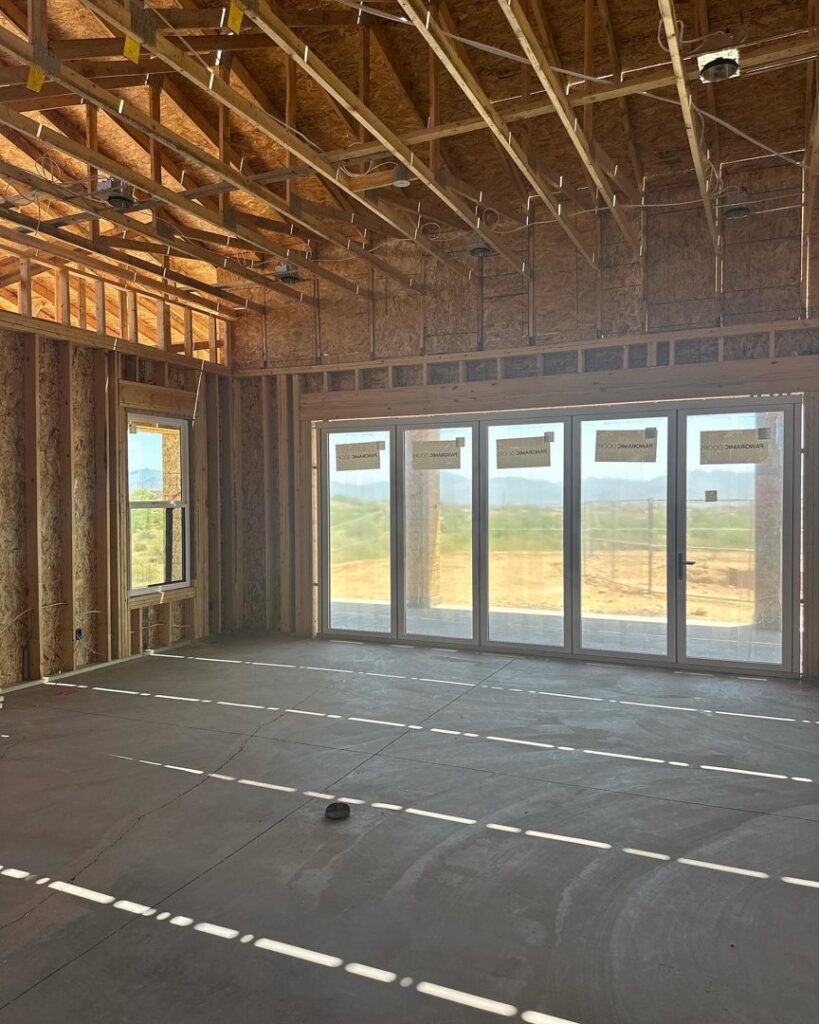 An interior view of a house under construction, featuring exposed wooden ceiling trusses and large folding doors, by Kelso Custom Builders, Inc. in Phoenix, AZ.