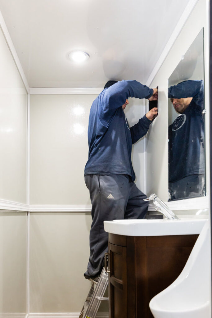 A worker installing interior fixtures above a mirror in a portable unit, a service provided by Comforts of Home Services Inc in Aurora, IL