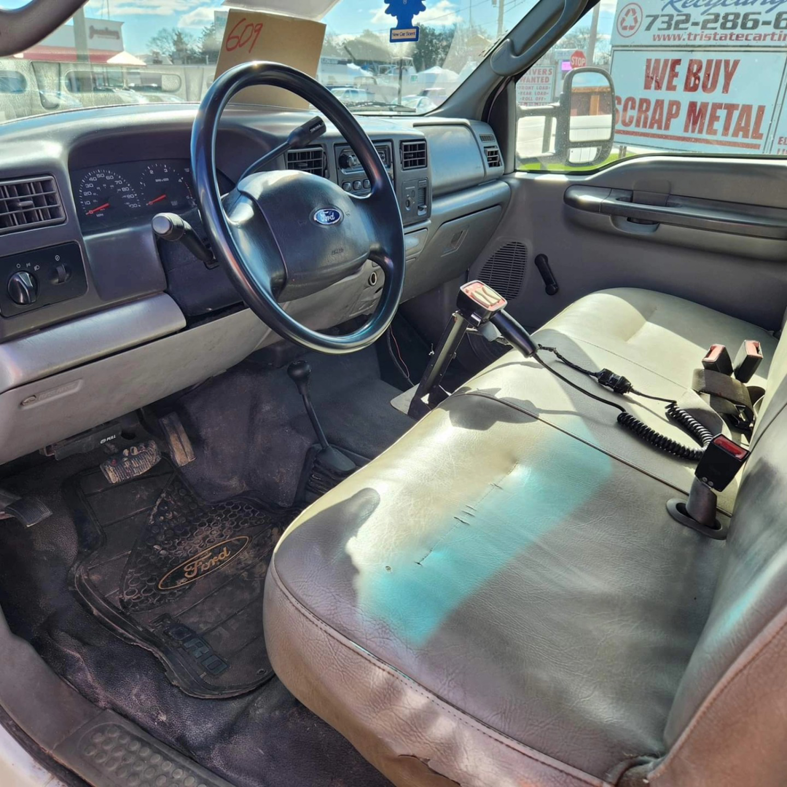 The interior of a Ford F450 junk removal truck, showing a sign for 'WE BUY SCRAP METAL' from Tri-State Carting, Inc in Bayville, NJ.