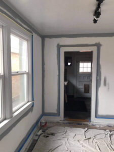 A room prepared for interior painting, with blue painter's tape on trim and drop cloths on the floor, by MDJ Handyman in Salt Lake City, UT.