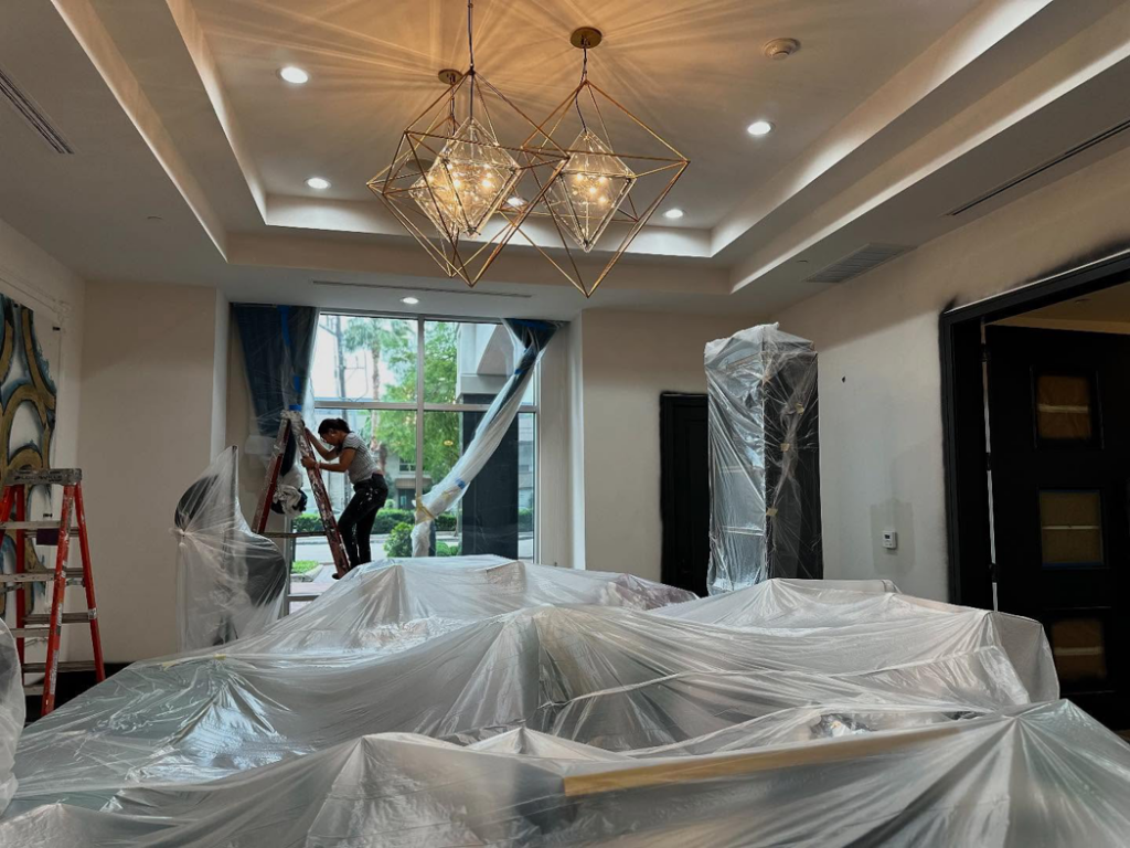 An interior painting project in progress with a worker on a ladder and covered furniture by Painting Services by David LLC in Houston, TX.