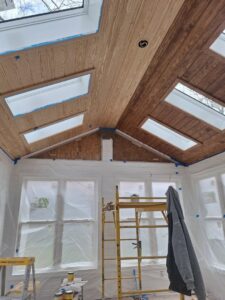 An interior room with a wooden plank ceiling and skylights, prepped for painting by Albis Morales Painting LLC in Raleigh, NC.