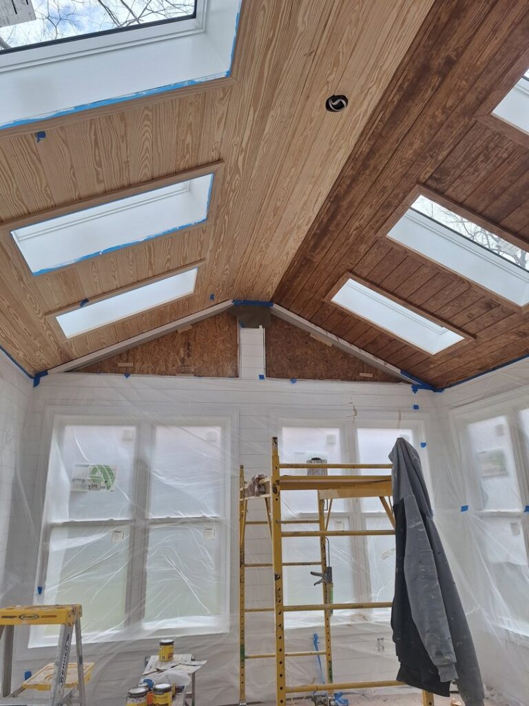 An interior room with a wooden plank ceiling and skylights, prepped for painting by Albis Morales Painting LLC in Raleigh, NC.