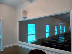 An interior wall with a large pass-through window, crown molding, and a wall-mounted speaker by Quiros Remodeling in Greenville, SC.