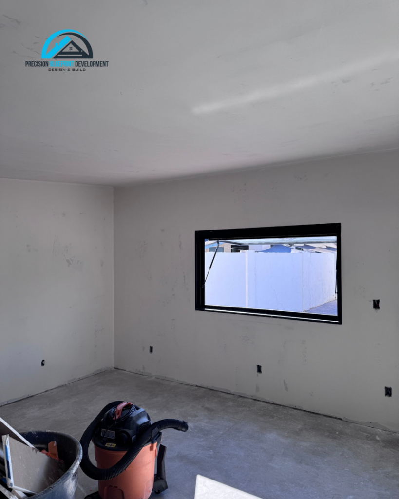 An interior room with newly installed drywall and a window, showing work in progress by Precision Blueprint Design & Development in San Tan Valley, AZ.