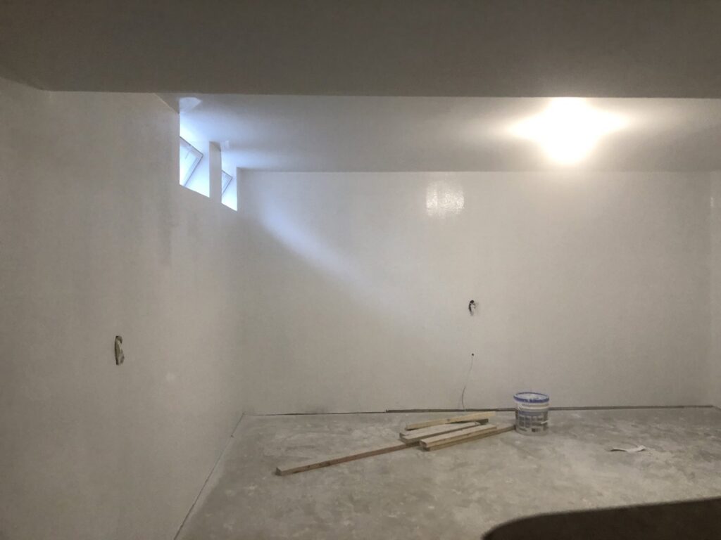 An empty room with freshly painted white walls and a concrete floor, showing interior painting work by Mp painting and roofing LLC in Dayton, OH