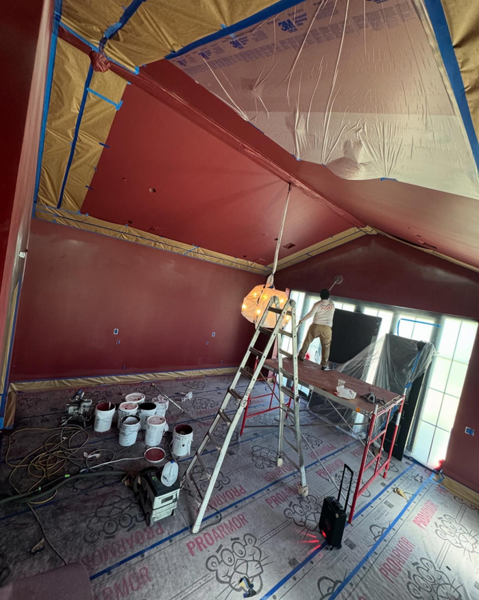 An interior room painting project in progress with a worker on scaffolding by Orange Door Custom Coatings in Phoenix, AZ.