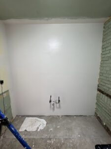 An interior room showing a wall partially painted white over green, with exposed pipes and a ladder, indicating work in progress by OG Renovations in Huntington, WV.